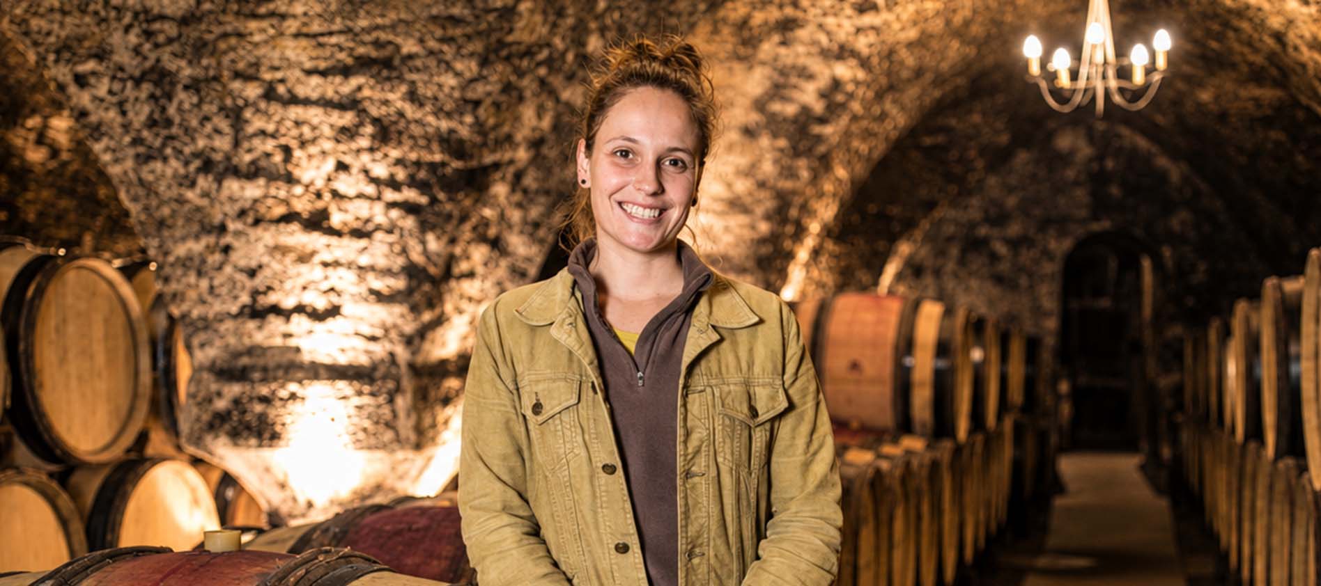 Winemaker standing in a wine cellar lined with oak barrels and illuminated stone arches